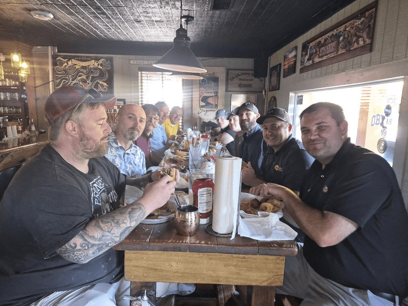 Ten men at a long community table eating lunch
